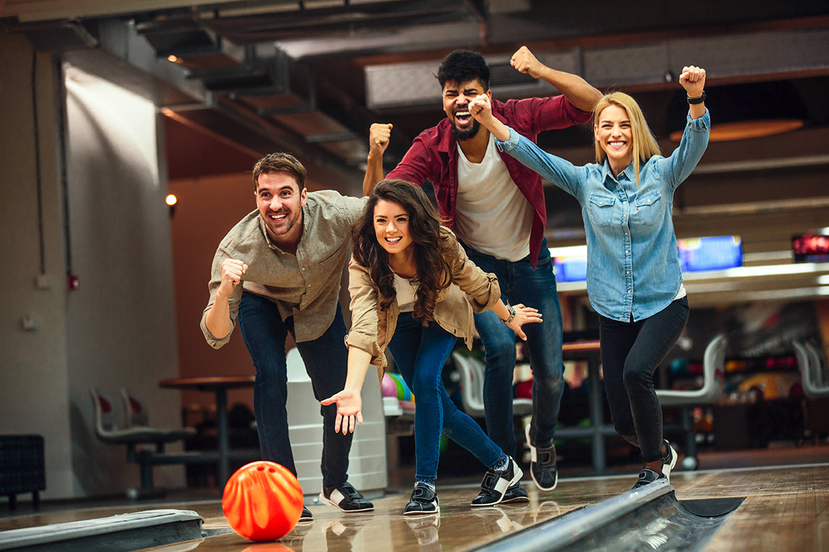 Shot of an attractive brunette throwing the bowling ball while her friends are cheering